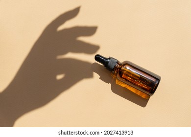 Mock-up of glass dropper bottle with hand shadow on brown background, in rays of sunlight. Concept of natural cosmetics. Close-up, flat lay, copy space