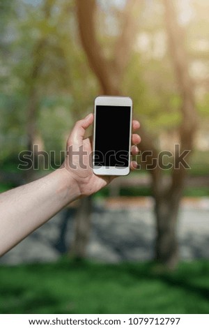 Mockup hands holding white smartphone on background of green trees. Place for text, design presentation website or app.