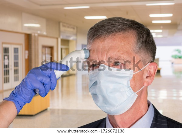 Stock image of a senior man having his temperature taken in a mall or office environment