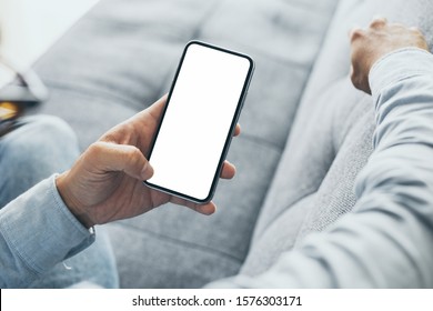 Mockup Image Blank White Screen Cell Phone.men Hand Holding Texting Using Mobile On Sofa At Home Office. Background Empty Space For Advertise Text.people Contact Marketing Business And Technology 
