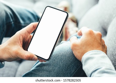 Mockup image blank white screen cell phone.men hand holding texting using mobile on  sofa at home. background empty space for advertise text.people contact marketing business and technology 