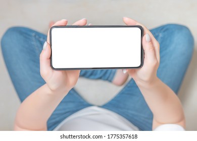 Mockup Image Blank White Screen Cell Phone. Female Hands Holding Texting Using Mobile Phone On Sofa At Home. Empty Space For Advertise Text. Young Woman In Jeans Looking At Smartphone Screen 