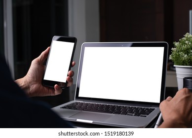 Mockup image, business man hand holding blank screen mobile smart phone, working on laptop computer with digital tablet on table in modern office for website or application design, over shoulder view
