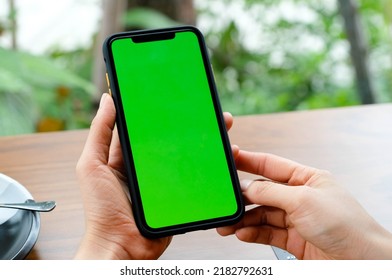 Mockup image of a business people holding smart mobile phone with blank green screen on vintage wooden table in modern cafe restaurant during meeting or lunch. - Powered by Shutterstock