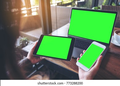 Mockup image of a businesswoman holding white mobile phone , black tablet and laptop with blank green screen on vintage wooden table with coffee cup in cafe - Powered by Shutterstock