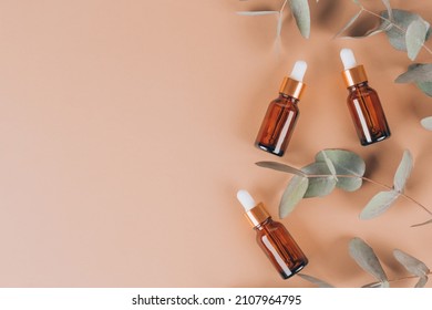 Mockup Image Of Glass Dropper Bottles With Eucalyptus Oil. Modern Organic Cosmetics, Facial Anti-aging Oil. Trendy Still Life Composition With Eucalyptus Leaves On Biege Background, Copy Space