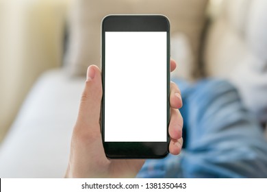 Mockup Image Of Hand Holding Black Mobile Phone With Blank White Screen. Student Lying On The Couch And Looks At The Vertically Positioned Smartphone Screen. Close Up.