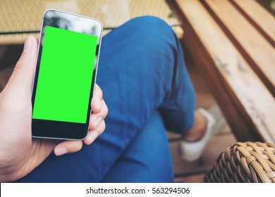 Mockup Image Of Hand Holding Black Mobile Phone With Blank Green Screen On Thigh With White Canvas Shoes