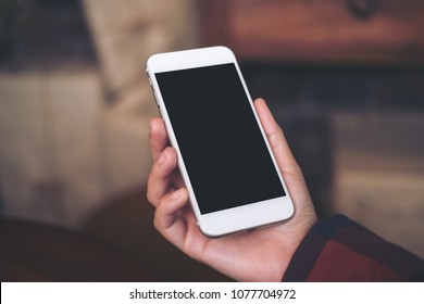 Mockup image of hand holding white mobile phone with blank black screen in cafe - Shutterstock ID 1077704972