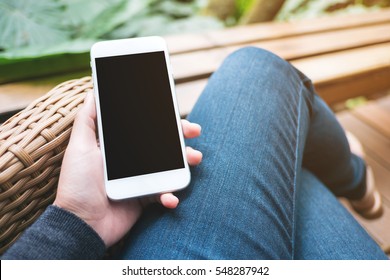 Mockup Image Of Hand Holding White Mobile Phone With Blank Black Screen On Thigh 