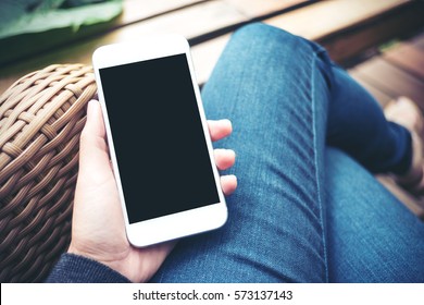 Mockup image of hand holding white mobile phone with blank black screen on thigh 