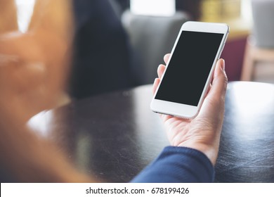 Mockup Image Of Hand Holding White Mobile Phone With Blank Black Screen On Table In Cafe