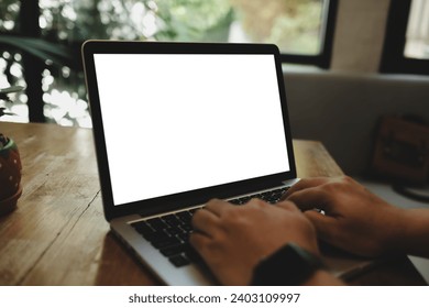 Mockup image of hand using laptop with blank white screen on vintage wooden table near glass windows in cafe