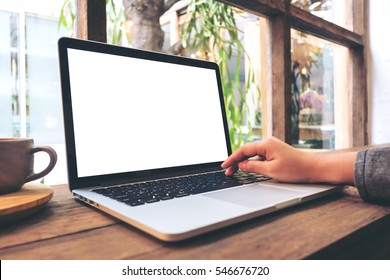 Mockup image of hand using laptop with blank white screen on vintage wooden table in cafe