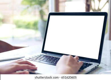 Mockup image of hand using laptop with blank white screen on vintage wooden table in cafe