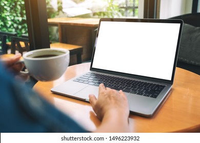 Mockup image of a hand using and touching on laptop touchpad with blank white desktop screen while drinking coffee