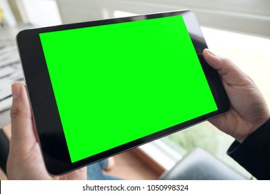 Mockup image of hands holding black tablet pc with blank green desktop screen in cafe