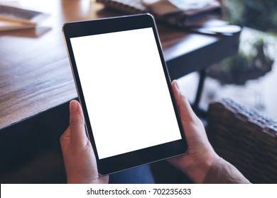 Mockup Image Of Hands Holding Black Tablet Pc With White Blank Screen On Wooden Table Background In Cafe