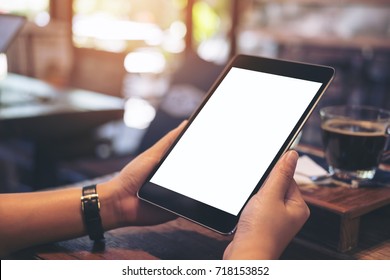 Mockup Image Of Hands Holding Black Tablet Pc With Blank White Screen With White Coffee Cup And Tea On Wooden Table In Cafe