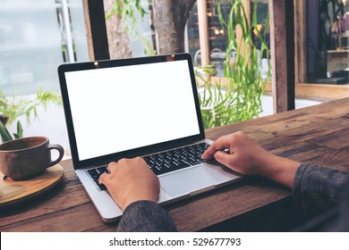 Mockup image of hands using laptop with blank white screen on vintage wooden table in cafe