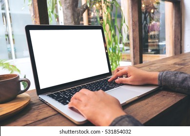 Mockup image of hands using laptop with blank white screen on vintage wooden table in cafe