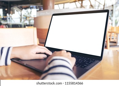 Mockup image of hands using and touching laptop with blank white desktop screen on wooden table in cafe