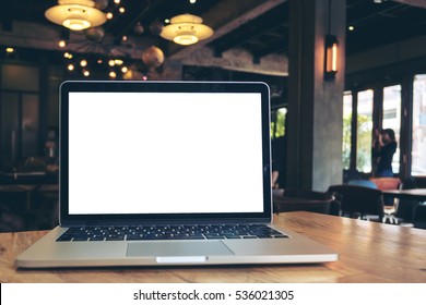 Mockup image of laptop with blank white screen on wooden table in dark modern cafe