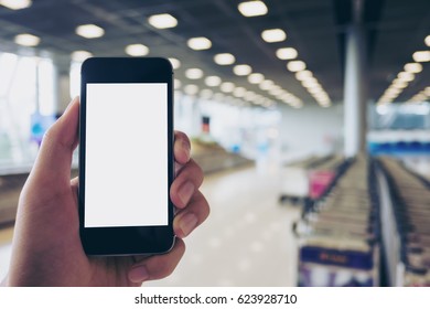 Mockup Image Of A Man Holding Black Mobile Phone With Blank White Screen While Standing And Waiting For Baggage Claim In The Airport