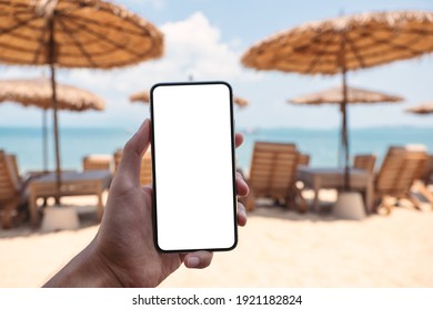 Mockup Image Of A Man Holding Mobile Phone With Blank Desktop Screen While Sitting On The Beach