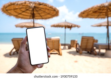 Mockup Image Of A Man Holding Mobile Phone With Blank Desktop Screen While Sitting On The Beach