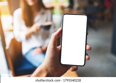 Mockup image of a man's hand holding mobile phone with blank white screen with woman drinking coffee in cafe