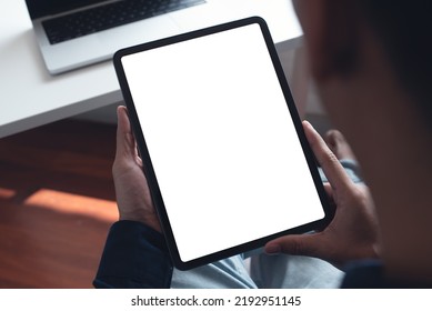 Mockup Image Of Man's Hand Holding Black Tablet Pc With Blank White Screen At Home Office, Over Shoulder View, Template