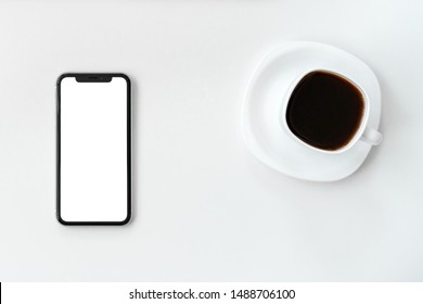 Mockup image of mobile phone with blank white screen and coffee cup with coffe on white table 