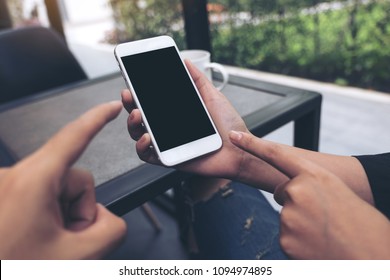 Mockup Image Of Two People Looking And Pointing At A White Mobile Phone With Blank Black Desktop Screen In Cafe