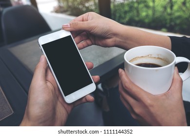 Mockup Image Of Two People Looking And Holding A White Mobile Phone With Blank Black Desktop Screen While Drinking Coffee In Cafe