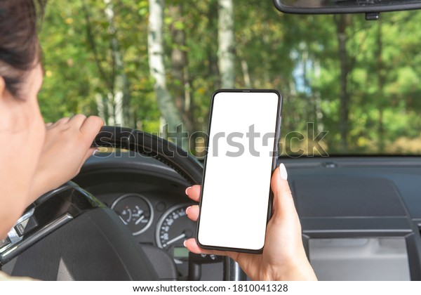 mockup image. woman driving a car\
holds a phone in her hand. woman holding blank screen cell phone\
while driving car. looks at your mockup phone while\
driving
