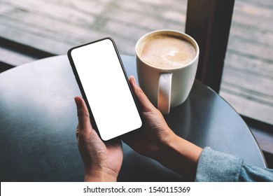 Mockup Image Of A Woman Holding Black Mobile Phone With Blank Screen With Coffee Cup On The Table