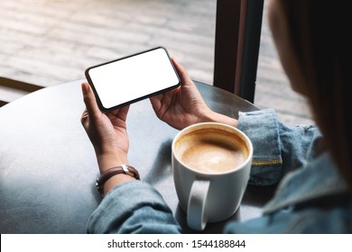 Mockup Image Of A Woman Holding Black Mobile Phone With Blank Screen With Coffee Cup On Wooden Table 