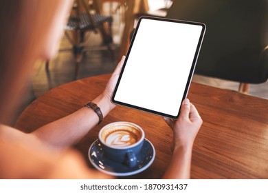 Mockup image of a woman holding digital tablet with blank white desktop screen with coffee cup on wooden table - Powered by Shutterstock