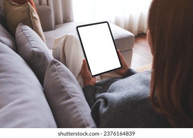 Mockup image of a woman holding digital tablet with blank desktop screen while lying on a sofa at home - Powered by Shutterstock