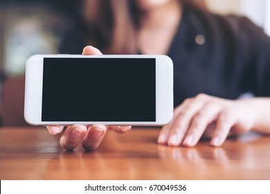 Mockup image of a woman holding and showing white horizontal mobile phone with blank black screen in restaurant 