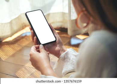 Mockup Image Of A Woman Holding And Using Black Mobile Phone With Blank Desktop Screen While Laying Down On The Floor With Feeling Relaxed