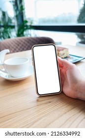 Mockup Image Of A Woman Holding And Using Black Mobile Phone With Blank Desktop Screen While Drinking Tea In Cafe.