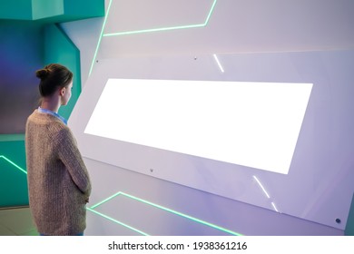 Mockup Image: Woman Looking At Blank Large White Interactive Wall Display At Modern Technology Exhibition, Museum, Trade Show. Mock Up, White Screen, Copyspace, Template, Education Concept