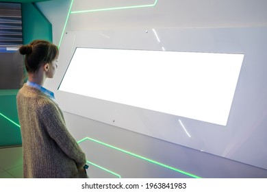 Mockup Image: Woman Looking At Blank Large White Interactive Wall Display At Modern Technology Exhibition, Museum, Trade Show. Mock Up, White Screen, Copyspace, Template, Education Concept