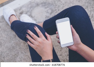 Mockup image of a woman sitting on the street and holding mobile phone with blank white screen    - Shutterstock ID 618708776