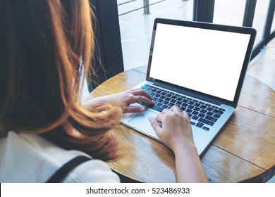 Mockup Image Of A Woman Using Laptop With Blank White Screen On Wooden Table In Modern Cafe