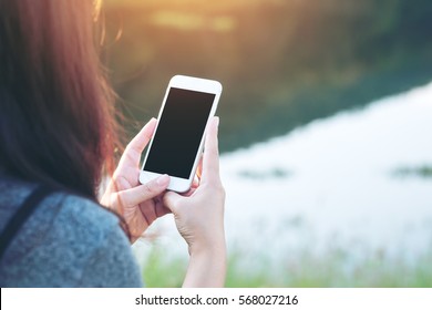 Mockup Image Of A Woman Using Smart Phone With Blank Black Screen At Outdoor And Lake Nature Background