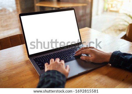 Mockup image of a woman using and typing on laptop computer with blank white desktop screen on wooden table