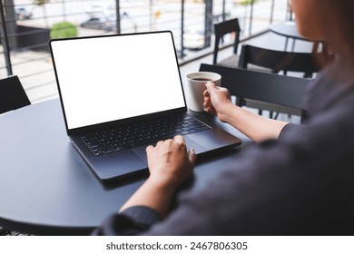 Mockup image of a woman working on laptop computer with blank white desktop screen while drinking coffee in cafe